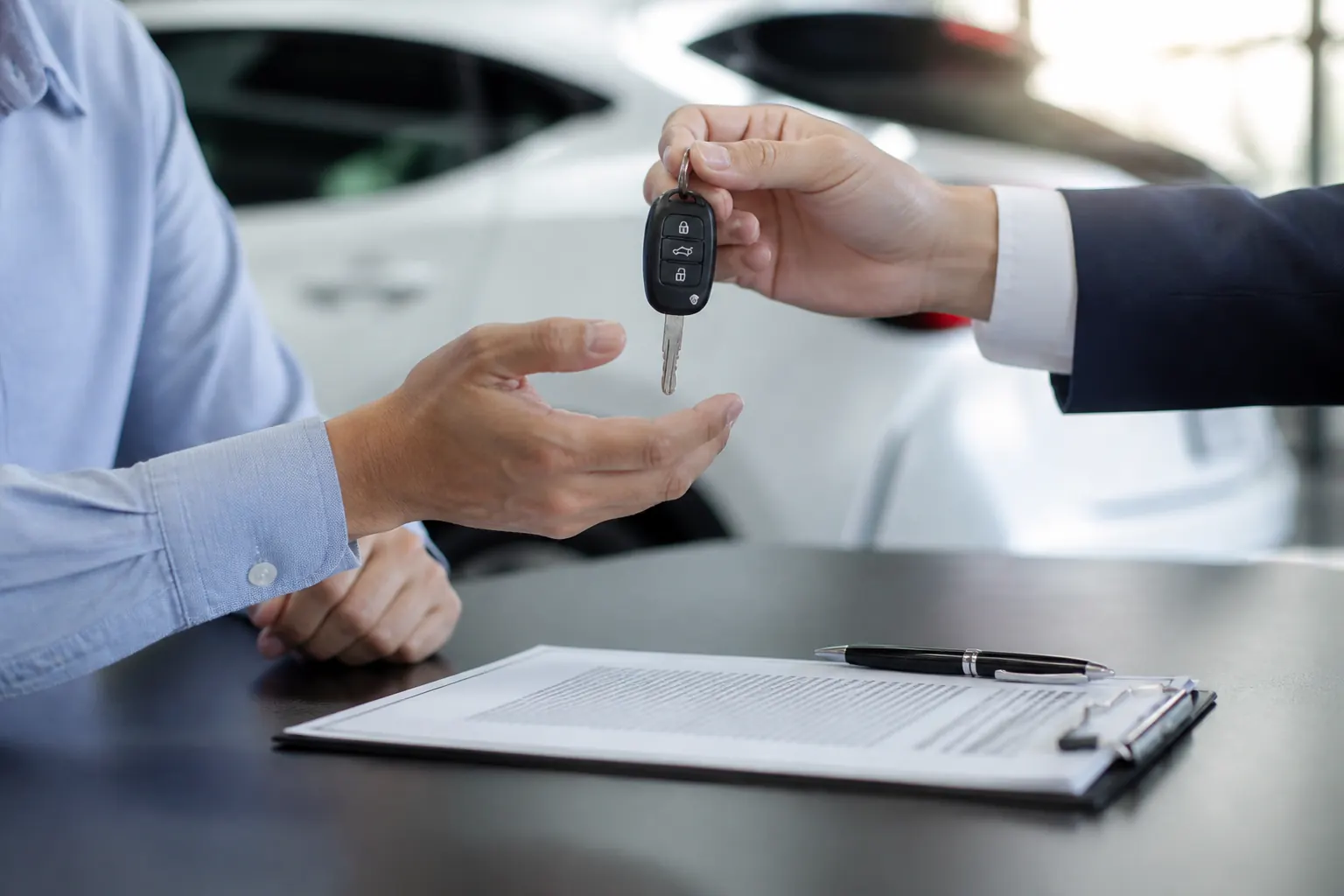 Two people exchanging car keys over signed paperwork